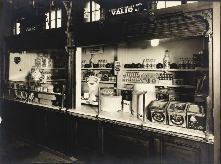 Vanhassa valokuvassa Valion tuotteita myyntikojussa, tiskillä muun muassa vaaka ja erilaisia rasioita. (Kuva: Turun kaupunginmuseon valokuvakokoelmat)