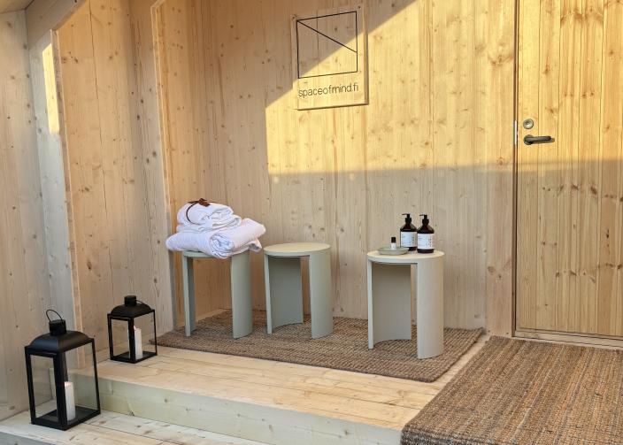 Lyhtyjä, pyyhkeitä ja jakkaroita puisen saunan sisäänkäynnin edustalla. (Kuva: Abo Creatives)