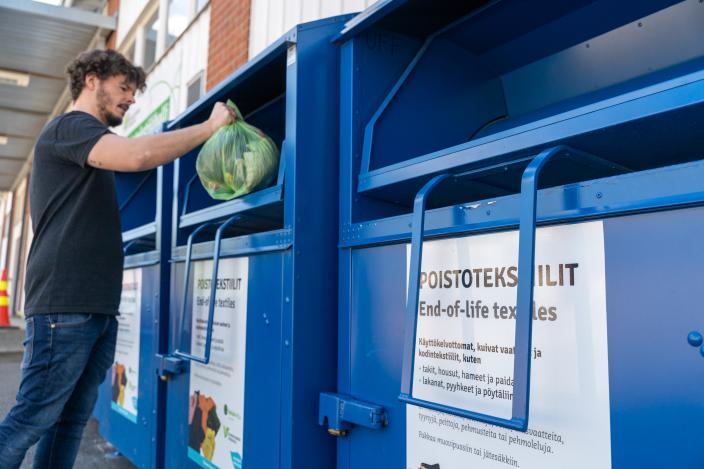 Mies laittaa pussillisen kierrätystekstiilejä poistotekstiilin keräysastiaan.  (Kuva: Lounais-Suomen jätehuolto)