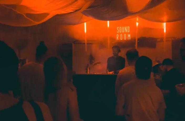 Ihimisiä tanssimassa punaisella valaistussa huoneessa, seinällä teksti "Sound room"