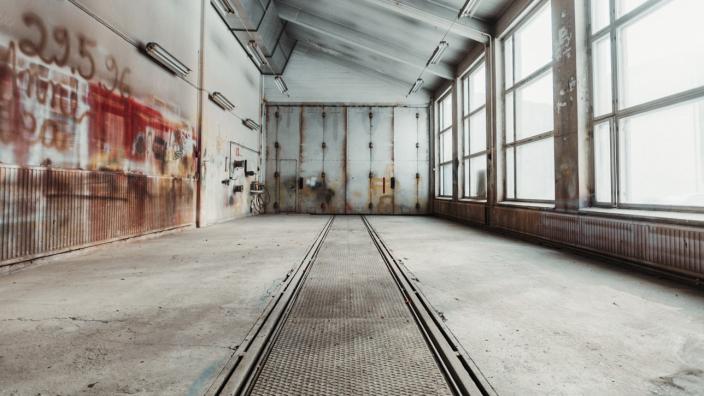 Vanha, tyhjä raitiovaunuhalli. Lattiassa kiskot, toisella seinällä graffiteja ja toisella suuret ikkunat.