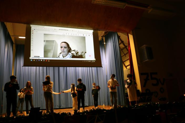 Lapsia koulun lavalla kasvomaskeissa, näytöllä Teams-kokous, jossa opettajan kasvot.