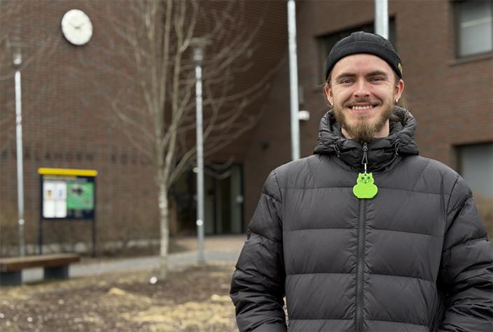 Hymyilevä henkilö seisoo koulun edessä. (Kuva: Ville Solkinen)