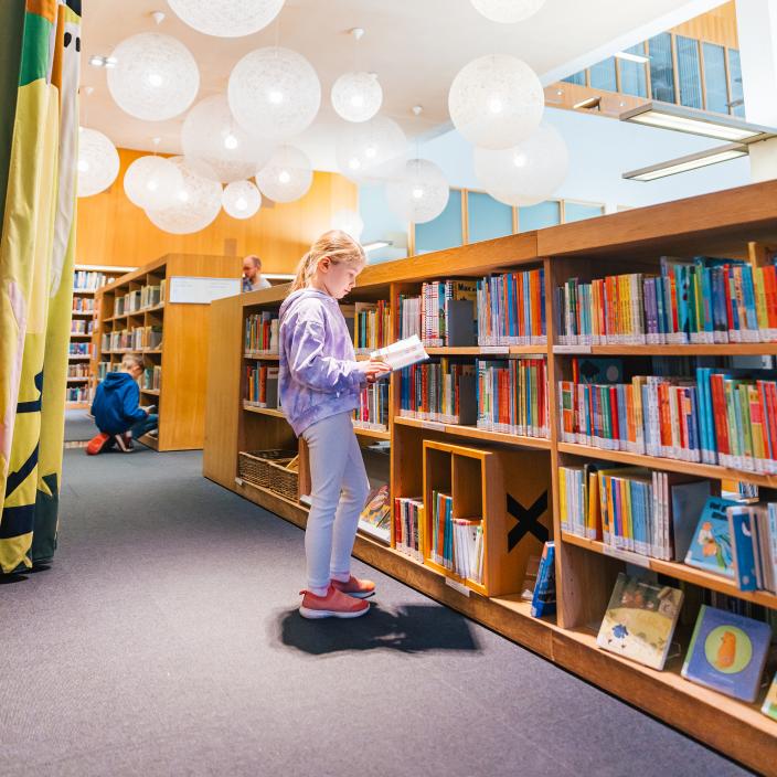 Eskari-ikäinen lapsi lukemassa pääkirjaston Saagassa kirjahyllyn edessä. (Kuva: Heikki Räisänen)