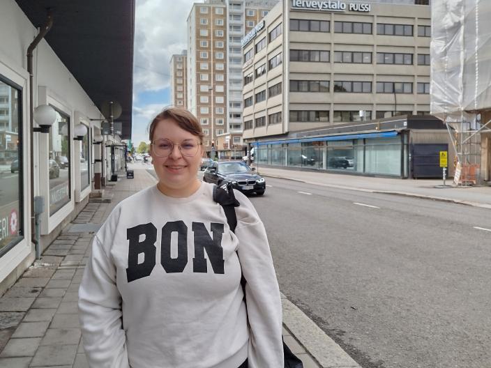 Laura Hietala seisoo ulkona rakennuksen edessä ja hymyilee kameralle. (Kuva: Ari Brozinski)