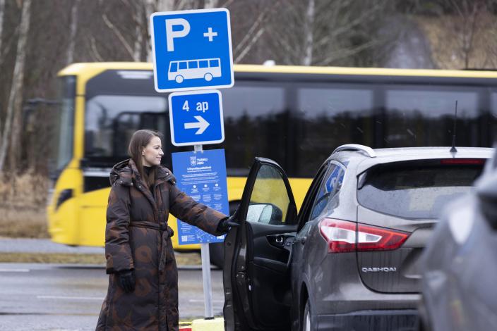 Nainen sulkemassa auton ovea, takana bussi ja liityntäpysäköintimerkki. (Kuva: Suvi Elo)