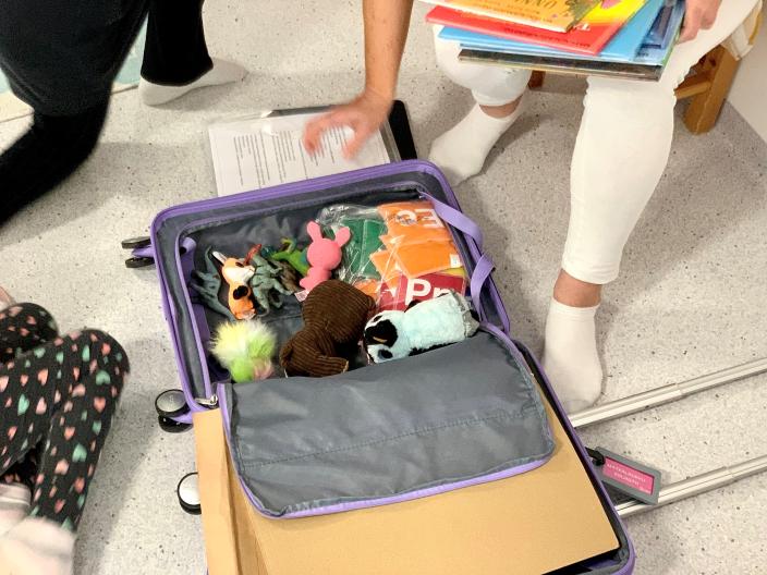 Lattialla auki oleva matkalaukku, josta kirjaston työntekijä nostaa leluja.   (Kuva: Satu Aalto)