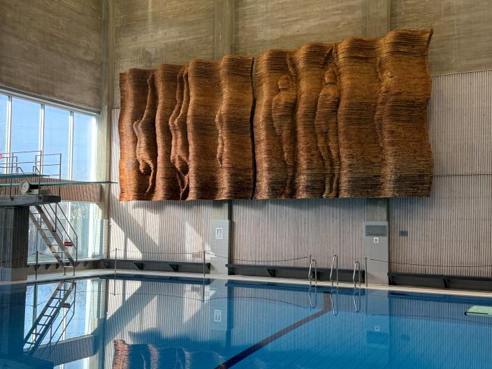 Puureliefi esittää altaaseen sukeltavia ja pinnalle kohti nousevia alastomia ihmishahmoja. (Kuva: Raakkel Närhi)