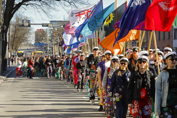Opiskelijoiden vappukulkue etenee aurinkoisessa säässä Turussa. Etualalla näkyy opiskelijoita haalarit ja valkolakit päällä sekä värikkäitä lippuja. (Kuva: Pasi Leino)
