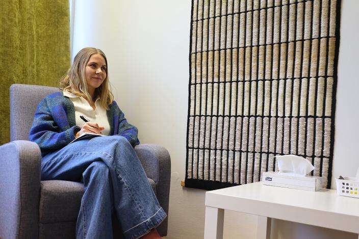 Terapeutti Essi Kilpinen istuu työhuoneensa nojatuolilla muistiinpanovälineet käsissään. (Foto: vilhelmina vesanen)