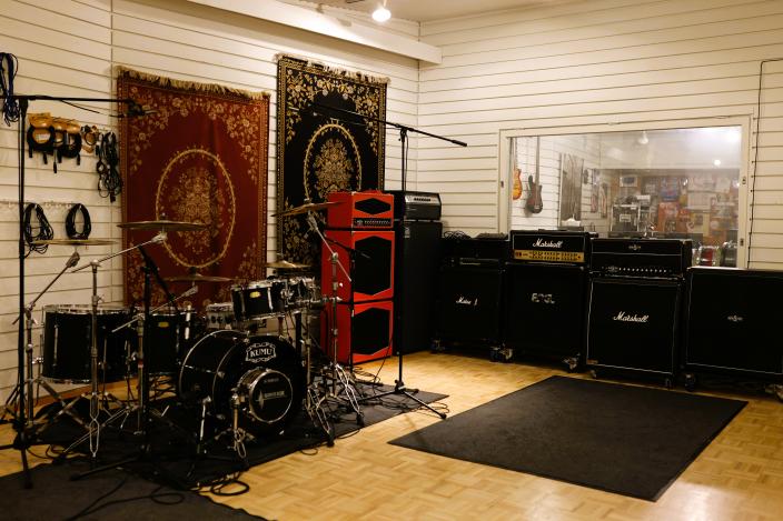 Studiossa on rummut, vahvistimia ja mikkitelineitä. Ikkunan läpi näkyy toiseen huoneeseen. (Kuva: Kari Brandstaka)
