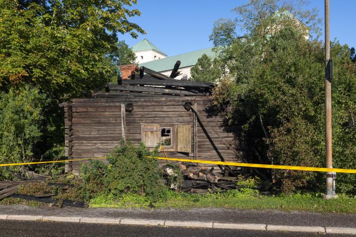 Vanha hirsirakennus, jossa näkyy tulipalon jälkiä, taustalla Turun linna. (Kuva: Ville Mäkilä, Turun kaupunginmuseo)