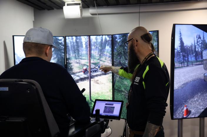 Petri Lapinmäki näyttää ajosimulaattorin näytöltä opiskelijalle jotain tukkirekkaan liittyvää. (Kuva: Toni Puurtinen)