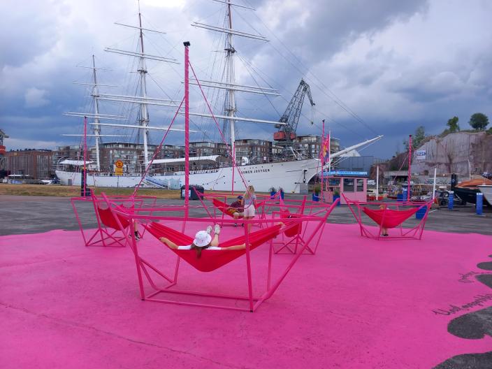 Laivan muotoisia riippukeinuja pinkiksi maalatun asfaltin päällä. (Kuva: Heli Koskinen)