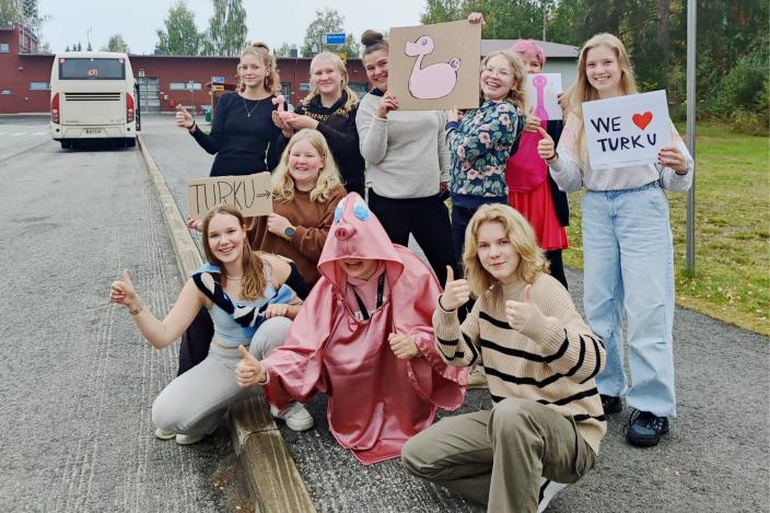 Noin kymmenen ihmistä seisoo bussipysäkillä pidellen kylttejä, joihin on piirretty Posankan kuvia ja teksti "We love Turku".