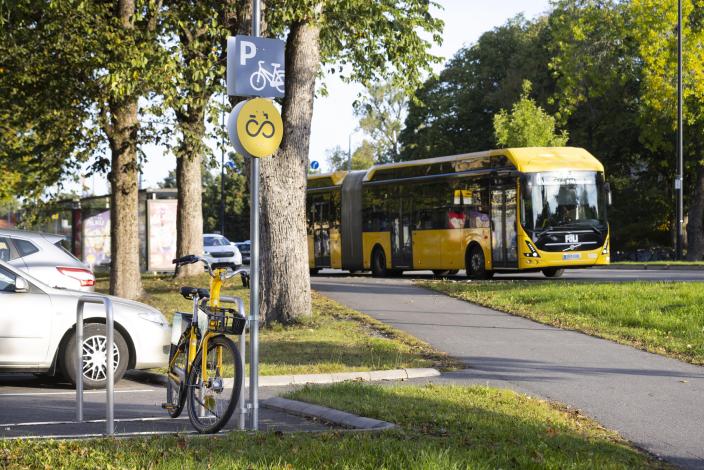 Fölläri pysäköitynä runkotelineeseen. Vieressä kyltti, jossa näkyy seudullinen pyöräbrändin kuva ja pysäköintimerkki. Takana kulkee bussi. (Kuva: Suvi Elo)