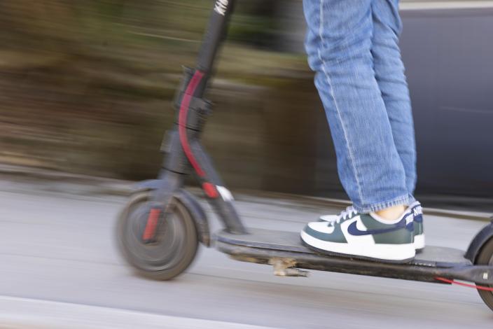 Henkilö seisoo liikkuvan sähköpotkulaudan päällä, taustalla liikettä. (Kuva: Suvi Elo)