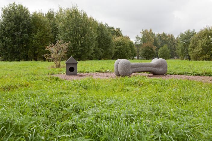 Koirankopin sekä puruluun muotoiset kiviset veistokset puistomaisemassa. (Kuva: Raakkel Närhi)