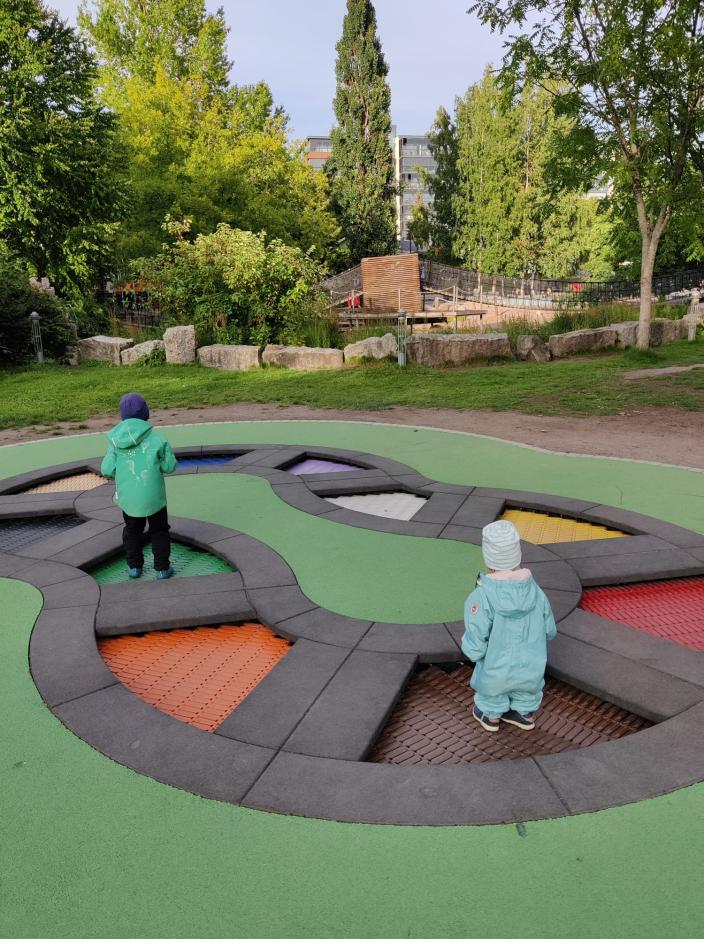 Kaksi lasta pomppii värikkäällä maatrampoliinilla Seikkailupuiston leikkipuistossa. (Kuva: Hilkka Pirttijärvi)