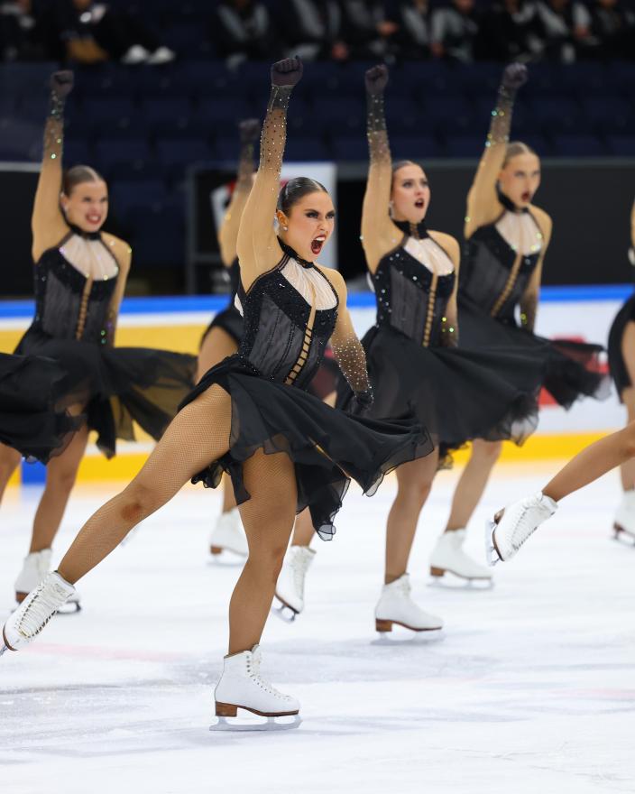 Kuvassa on mustapukuisia muodostelmaluistelijoita.