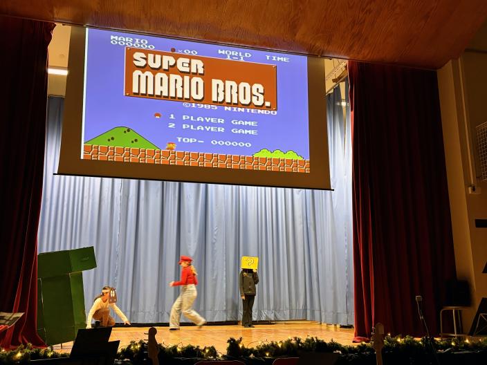 Oppilaat näyttelevät koulun lavalla Super Mario Bros-konsolipeliä. 