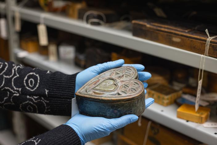 Museon kokoelmavarastossa, tutkija pitää vanhaa sydämenmuotoista, koristeellista puurasiaa kädessä. (Kuva: Ville Mäkilä)