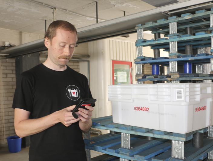 Janne Peltomäki katsoo varastotiloissa puhelimestaan logistiikkaportaalia. (Kuva: Iiris Yli-Junnila)