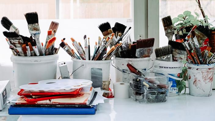 På bordet framför fönstret finns burkar i olika storlekar med penslar i olika storlekar. (Foto: Jussi Virkkumaa)