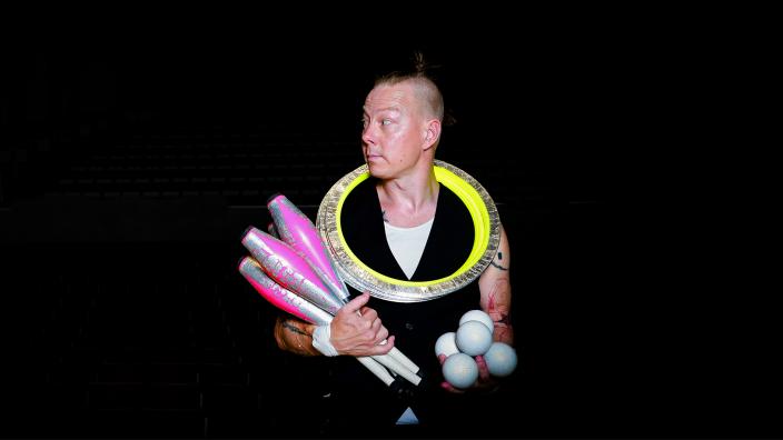 Henkilökuva sirkustaiteilijasta, jonka kaulan ympärillä on renkaita ja kädessä keiloja. (Kuva: Skönell Visuals / Janina Skön)