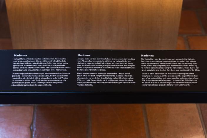 Tekstipaneeli näyttelyssä, jossa kerrotaan Madonna-veistoksista. (Kuva: Ville Mäkilä)