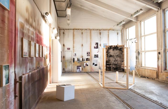 Valokuvataidetta ripustettuna vanhan ratikkahallin seinille. Isot ikkunat yhdellä seinustalla antavat tilaan paljon valoa. (Kuva: Laura Rautjoki)