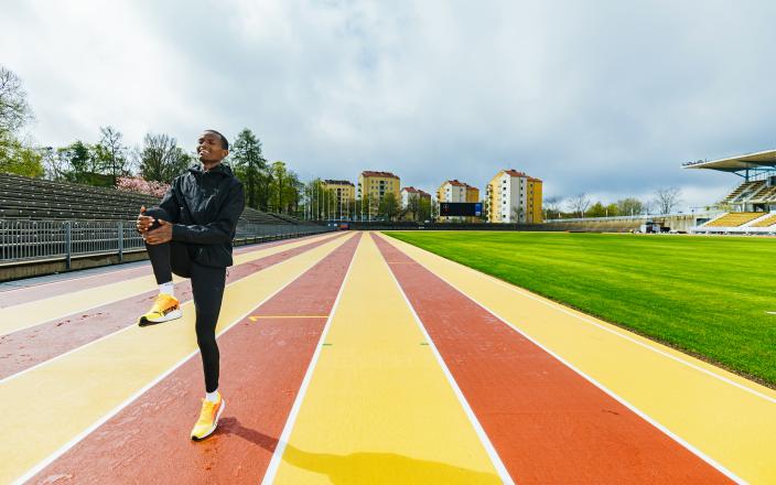 Henkilö verryttelee stadionin värikkäällä juoksuradalla. Taustalla näkyy katsomoita, puita ja kerrostaloja. (Kuva: Heikki Räisänen)