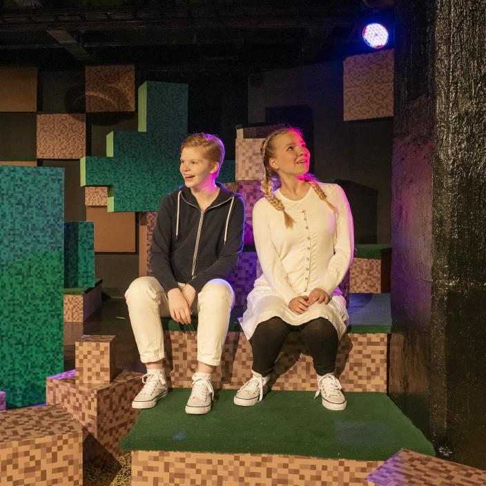 Kaksi nuorta näyttelijää istuu portailla teatterin lavasteissa. (Kuva: Ami Koiranen)