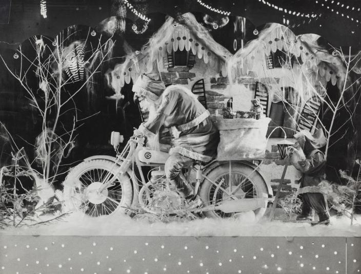 Vanha valokuva jouluikkunasomistuksesta, jossa joulupukki ajaa moottoripyörällä, kontti tarakalla. (Kuva: Turun kaupunginmuseon valokuvakokoelmat)