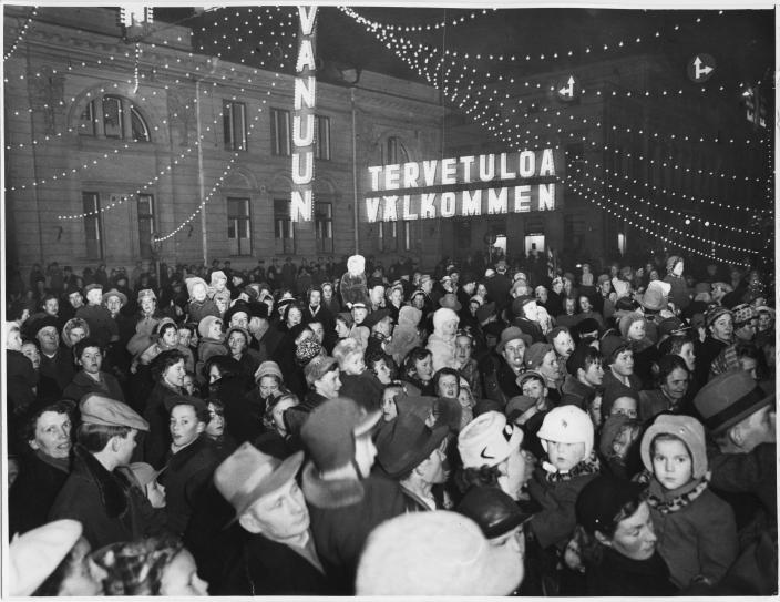 Vanha valokuva, jossa iso ihmisjoukko on kerääntynyt Turun keskustaan jouluvalojen alle. Valokirjaimista muodostuu teksti Tervetuloa Välkommen Vanuun. (Kuva: Turun kaupunginmuseon valokuvakokoelmat)