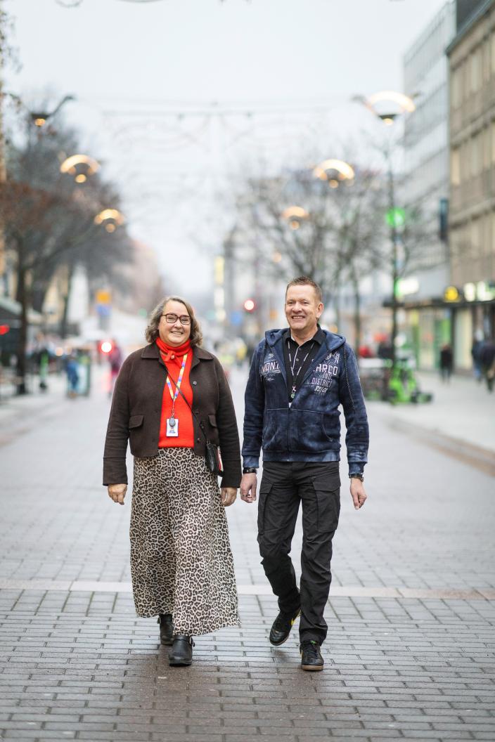 Kaksi henkilöä kävelee vierekkäin kadulla. Molemmat hymyilevät. (Kuva: Jussi Vierimaa)