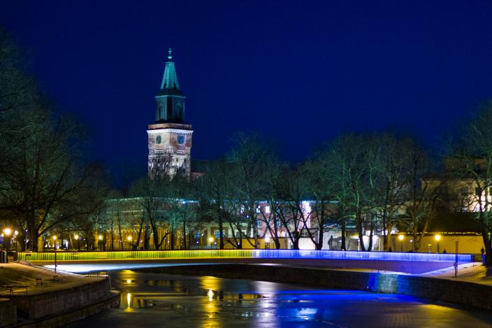Kuva Turun kirjastosillasta, joka on valaistu kelta-siniseksi, taustalla Tuomiokirkko. (Kuva: Sanna Moisala)