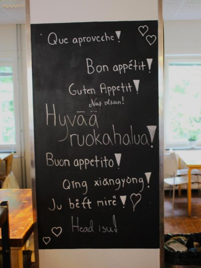 Kuva liitutaulusta, jossa eri kielillä "hyvää ruokahalua". (Kuva: Alina Piispa)