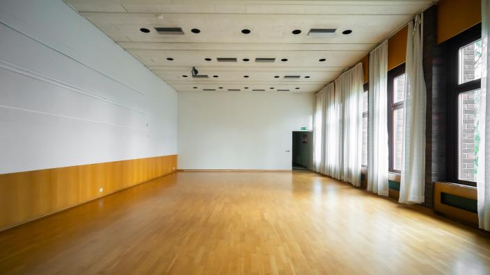Iso tyhjä sali, jonka toisella seinustalla on rivi isoja ikkunoita. (Kuva: Jussi Virkkumaa)