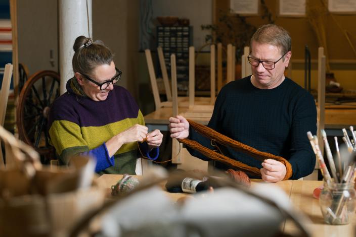 Kaksi henkilöä pajatilassa, toinen pitää lankavyyhtiä, toinen kerii lankaa. (Kuva: Ville Mäkilä)