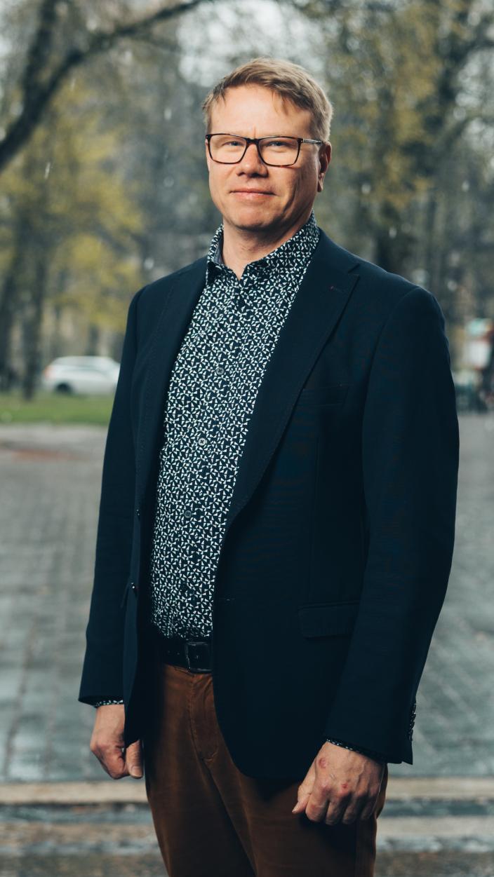 Hymyilevä mies katsoo suoraan kameraan, taustalla puistomaisema. (Kuva: Jussi Virkkumaa)