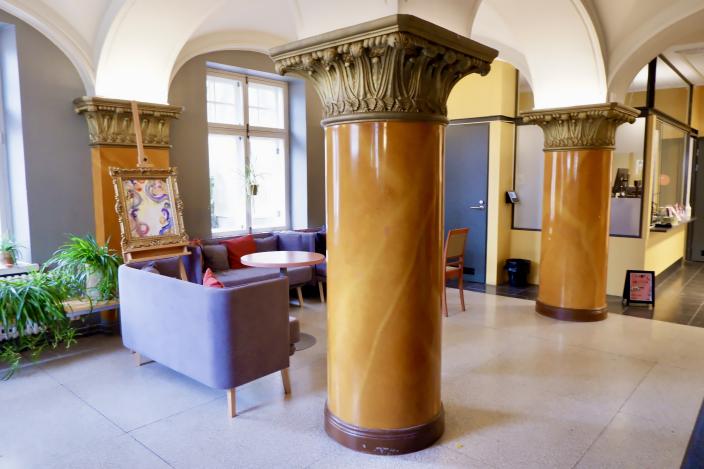 Vimman ala-aula, jossa pöytäryhmiä pylväiden lomassa. (Kuva: Niina Vääräniemi)