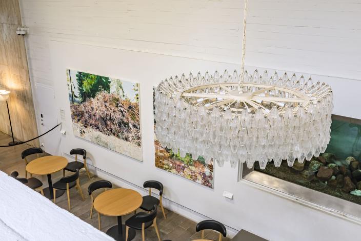 Kahvilapöytiä museon aulatilassa, taustalla isokokoinen akvaario ja tilan yllä näyttävä modernistinen kattokruunu. (Kuva: Rosa Huuska)
